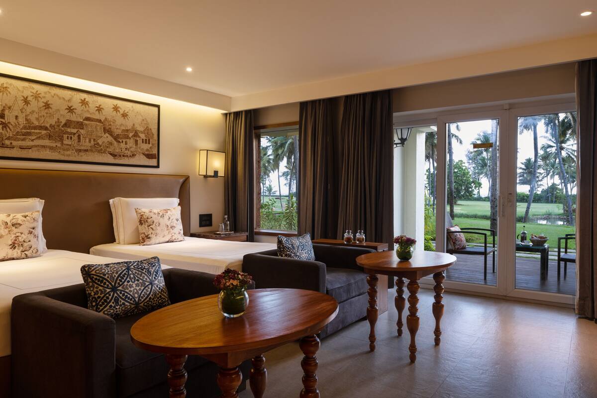 Habitación de hotel con una cama grande, dos sofás, una mesa de centro y vistas a un paisaje tropical a través de la puerta de cristal.