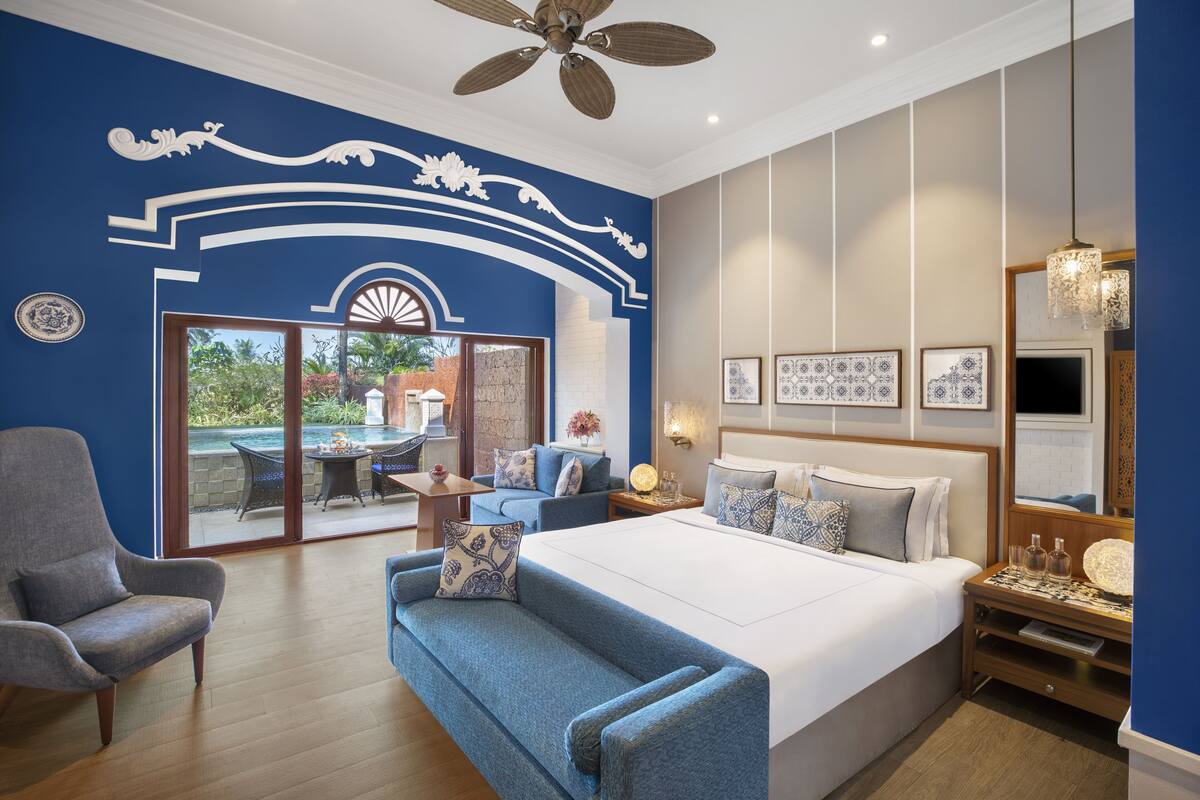 Un dormitorio con una cama grande, un sofá, una silla, un comedor con mesa y sillas, y vistas al exterior.