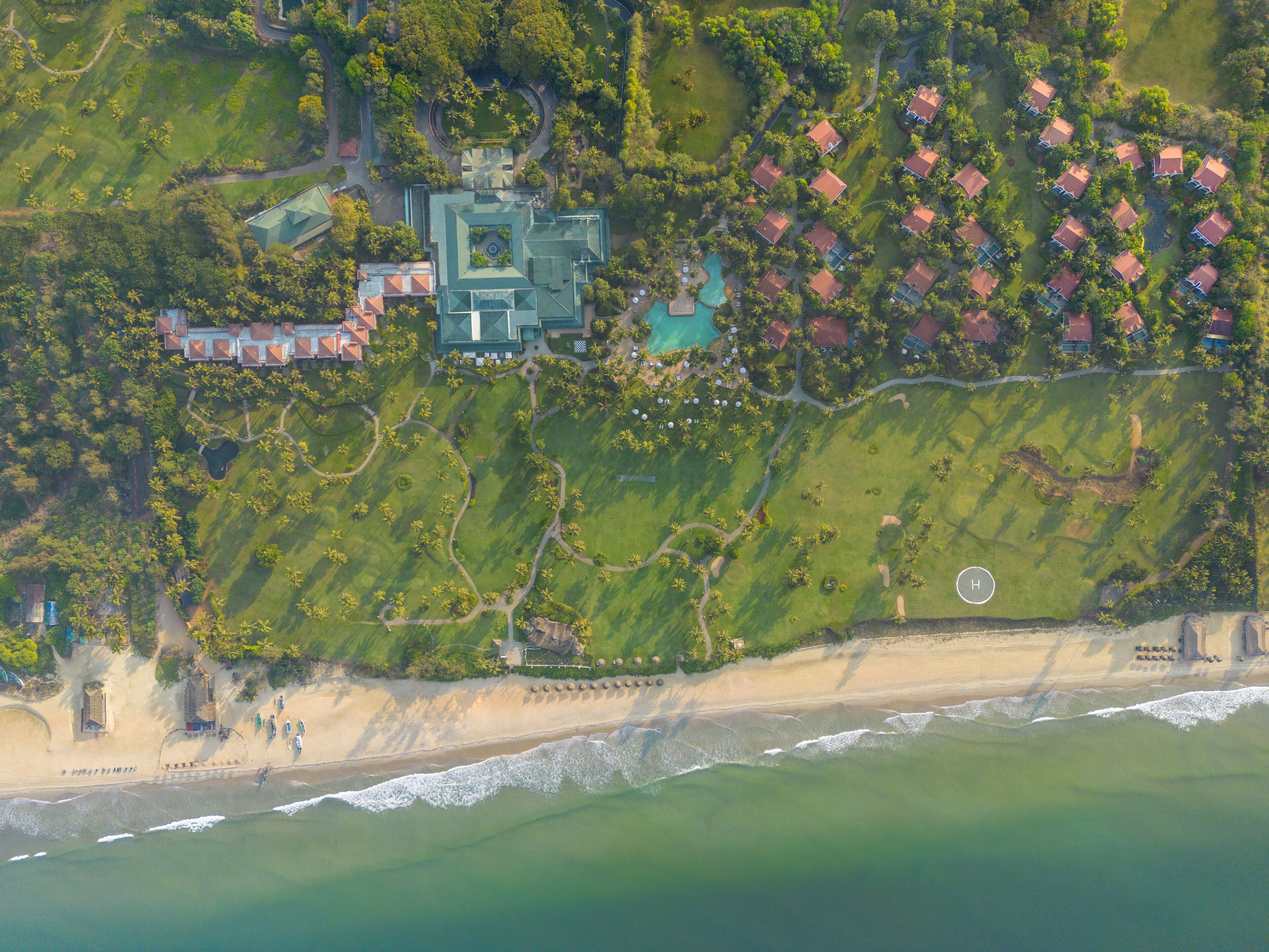An aerial view of a coastal resort with a large central building, multiple bungalow-style houses, and a beachfront.