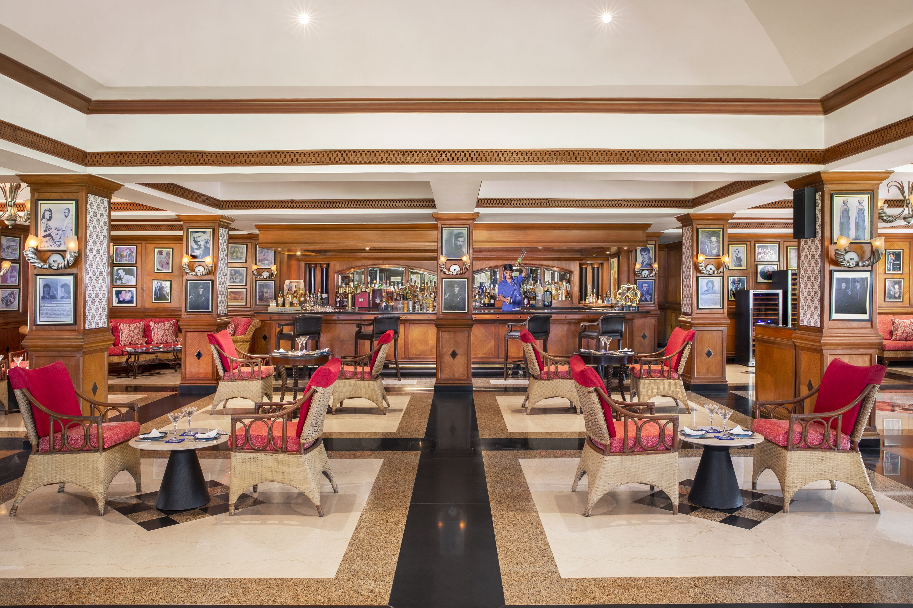 A spacious lobby with a central bar, multiple seating areas, and a checkered floor pattern.