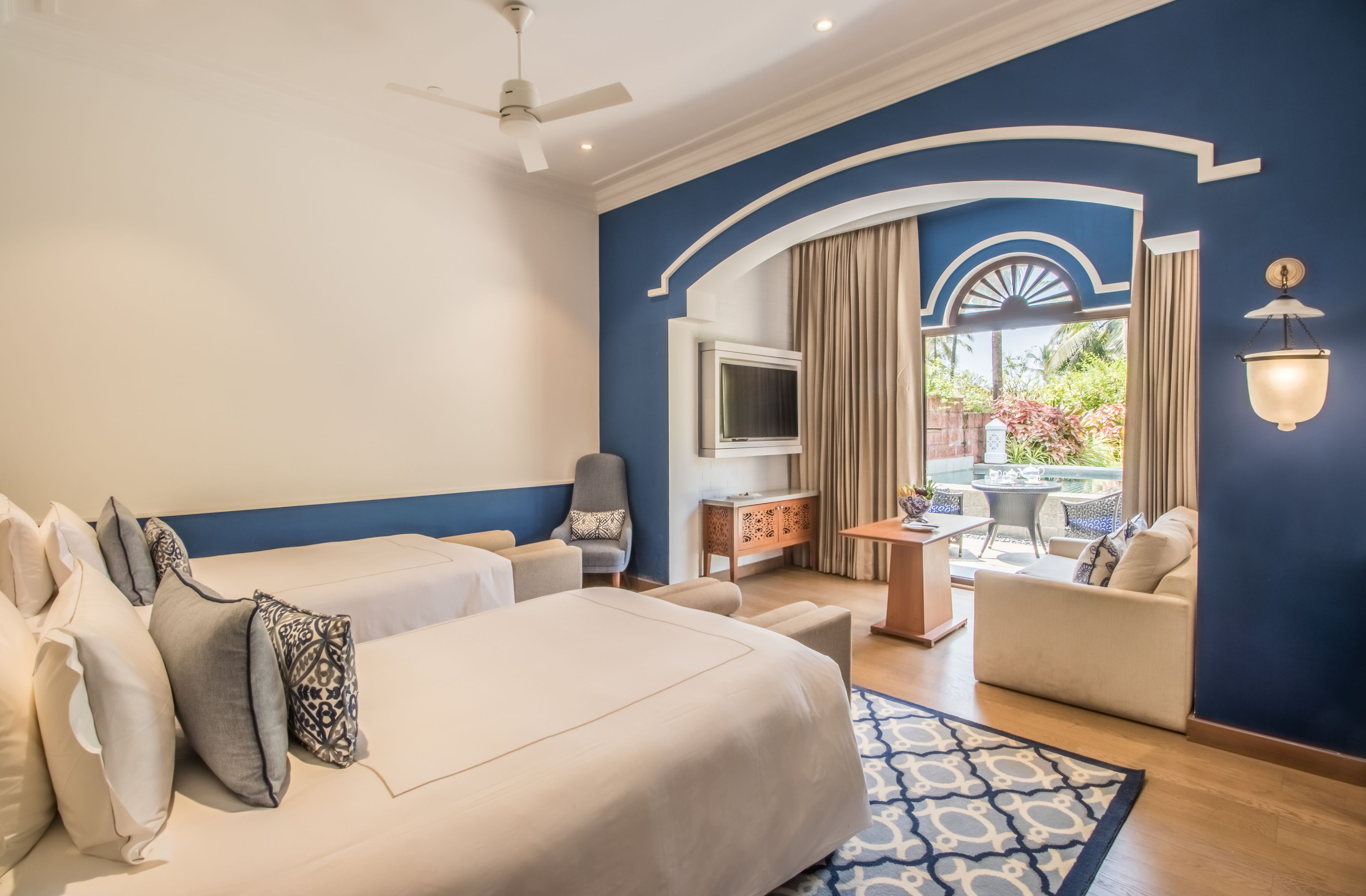 Habitación de hotel con una cama grande, un sofá, televisión y un balcón con mobiliario de exterior.
