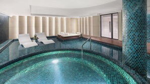 Un área de piscina interior moderna con diseño de baldosas hexagonales, sillas de descanso y una zona de estar con vistas a la piscina.