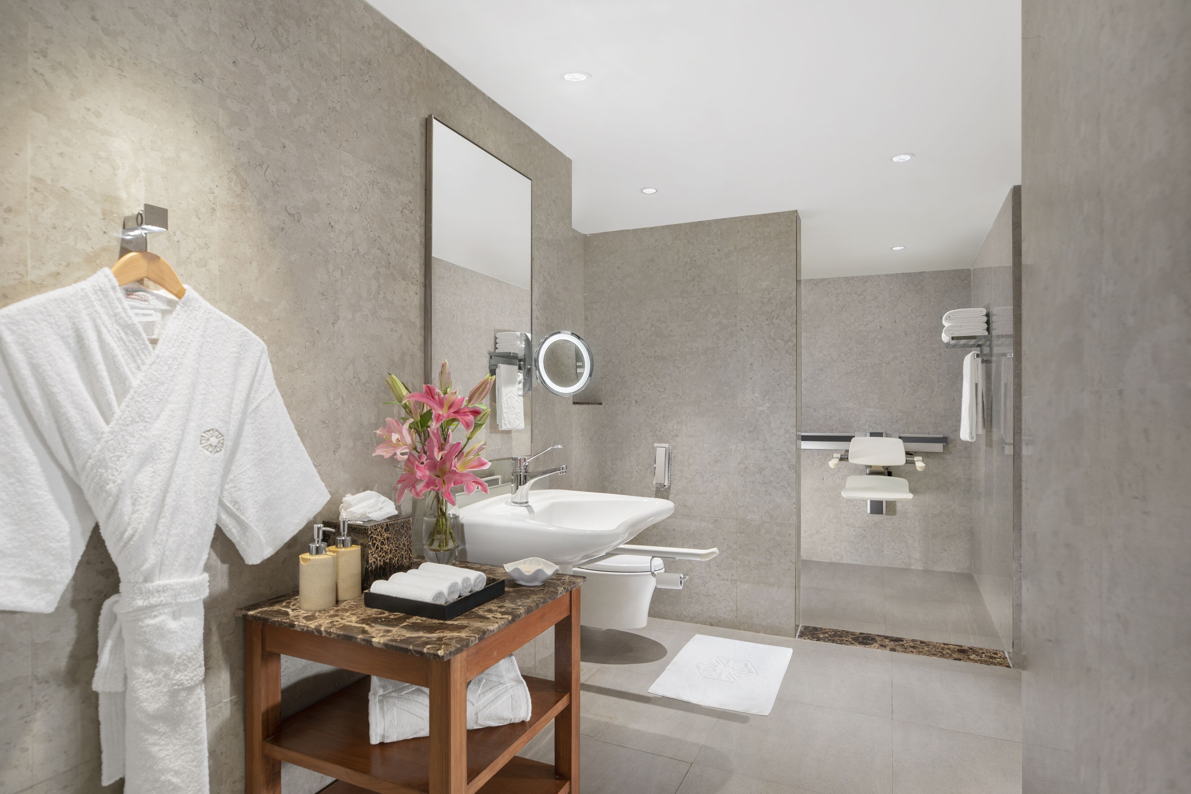 A modern bathroom with a marble vanity, a large mirror, a toilet, and a shower area.