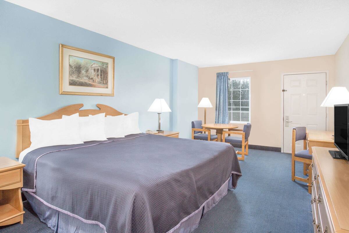 Une chambre d’hôtel avec un grand lit, deux tables de chevet, un bureau avec une chaise, une télévision et un tableau encadré au mur.