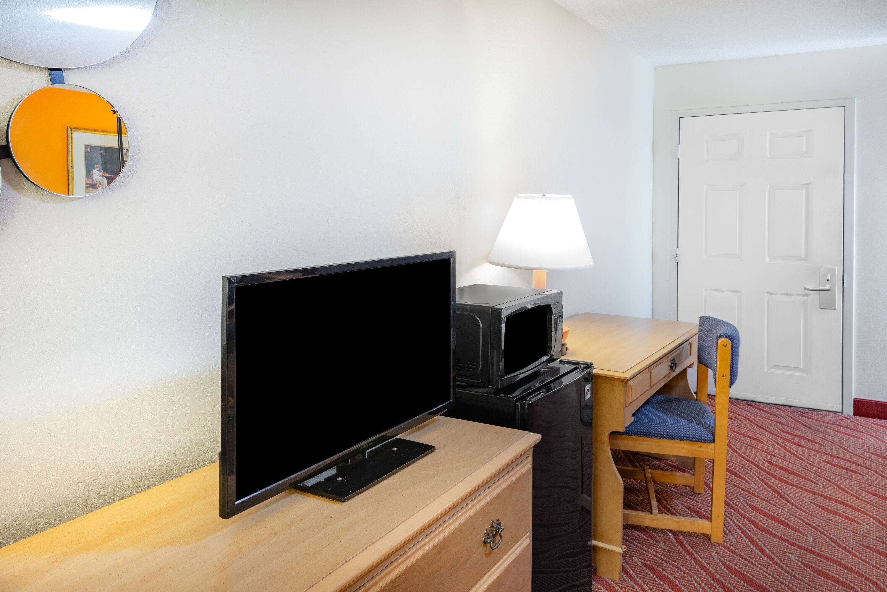 Ein Hotelzimmer mit Holzschreibtisch, Fernseher, Lampe, Stuhl und Tür.