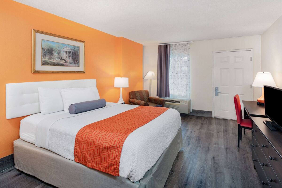Une chambre d’hôtel comprenant un lit, deux lampes de chevet, une télévision, un bureau avec une chaise et une porte.