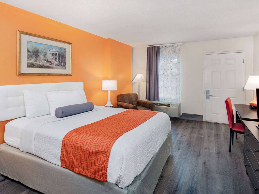 A hotel room with a bed, two bedside lamps, a television, a desk with a chair, and a door.