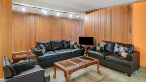 Un salón con un sofá de cuero oscuro, una mesa de centro de vidrio y paneles de madera en las paredes.