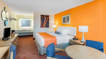 A hotel room with a bed, a desk, a chair, a table, and a lamp.