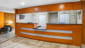 Un área de recepción con un mostrador de madera, una zona de estar con una lámpara y un piso de baldosas.