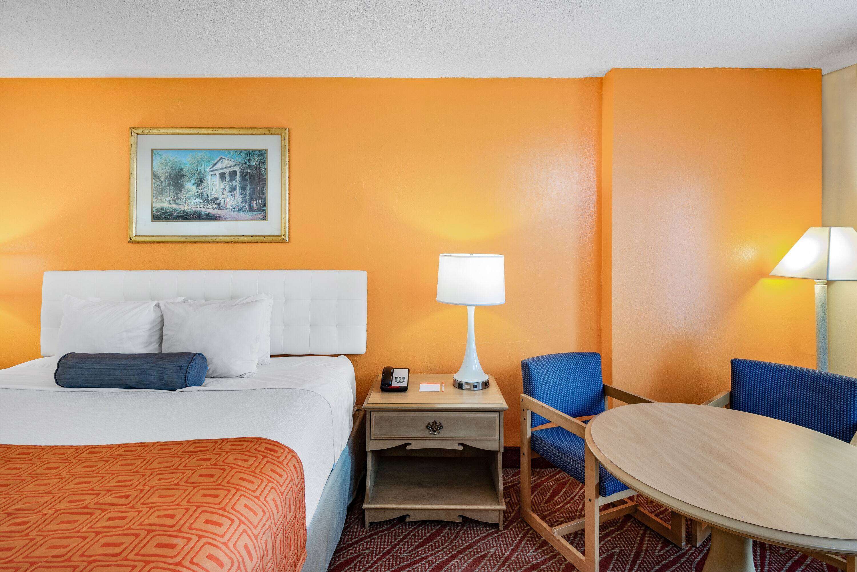 A hotel room with a bed, a nightstand with a lamp, a chair, and a small table.