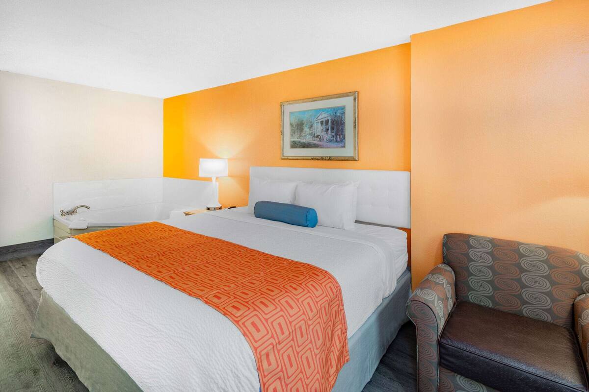 Une chambre d’hôtel avec un grand lit, une table de chevet avec une lampe, une chaise et un tableau au mur.