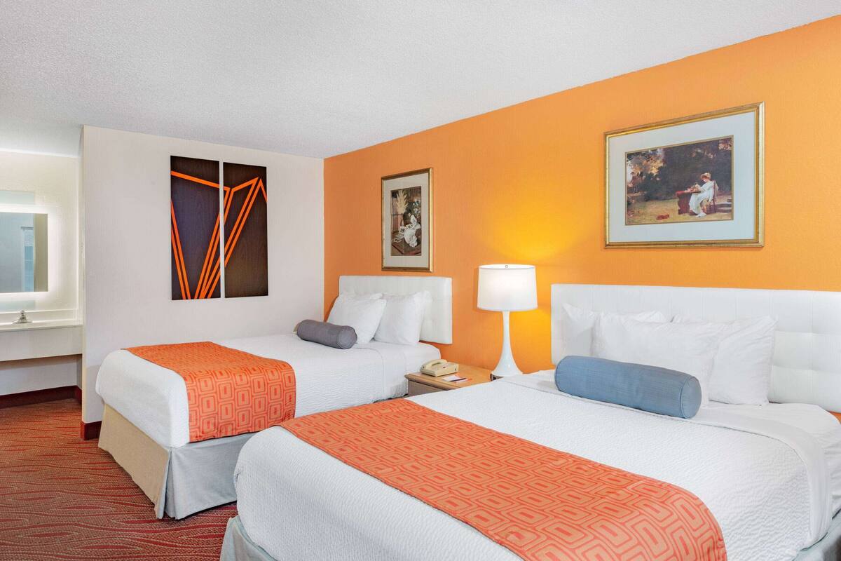 Une chambre d’hôtel avec deux lits, une table de chevet, une lampe et des œuvres d’art accrochées aux murs.