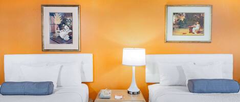 A hotel room with two beds, a nightstand with a lamp, and two framed pictures on the wall.