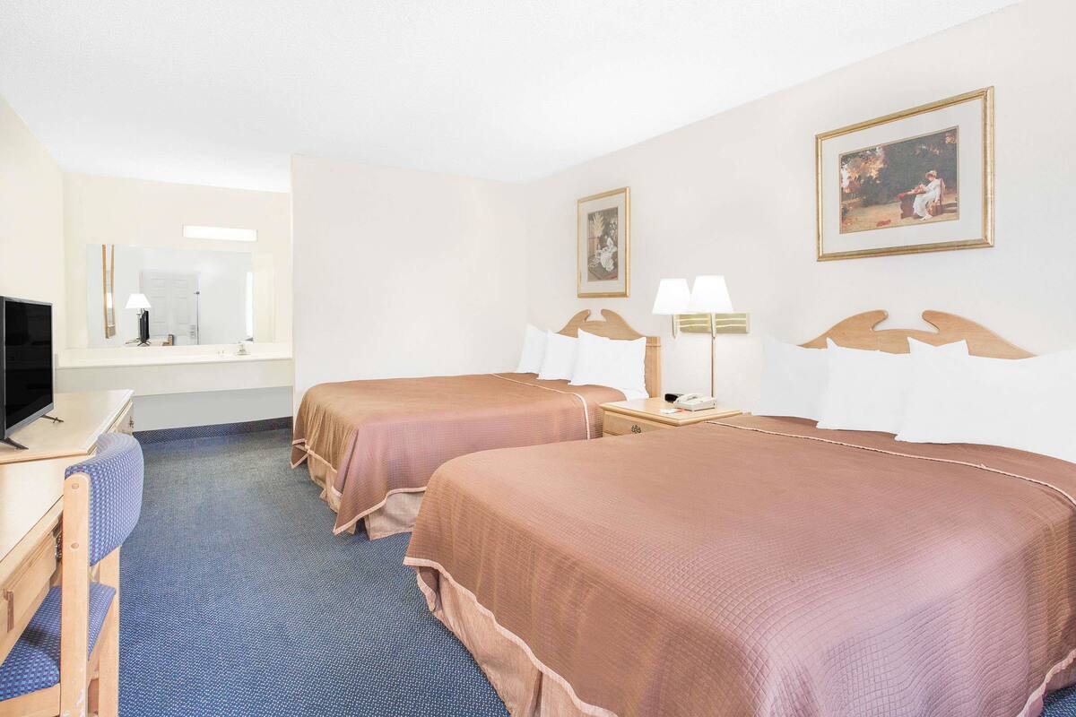 Une chambre d’hôtel avec deux lits, un bureau avec un ordinateur, un miroir et deux lampes de chevet.