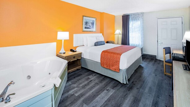 Habitación de hotel con cama, mesita de noche, escritorio, silla, ventana con cortinas y puerta.