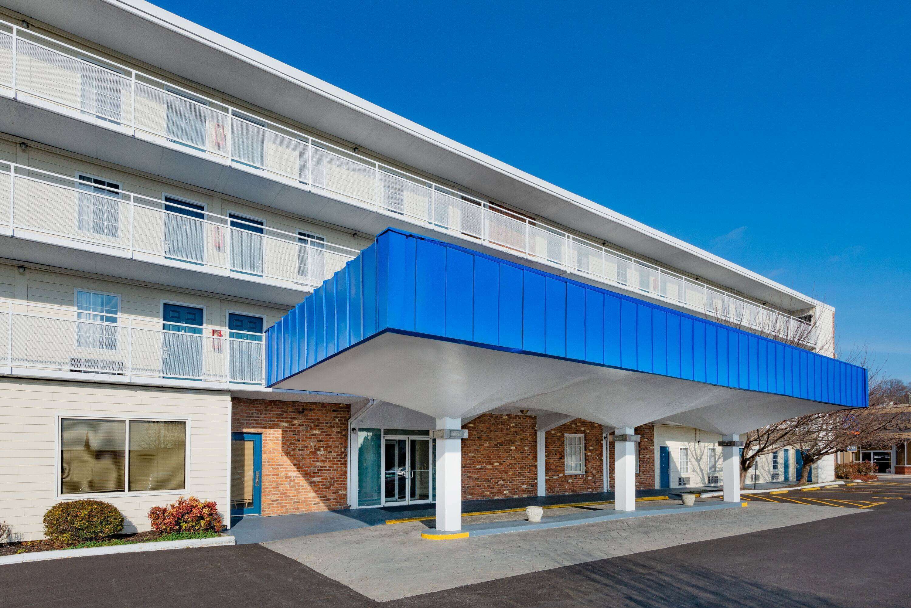 A multi-story hotel with a covered outdoor area, a brick facade, and a parking lot.