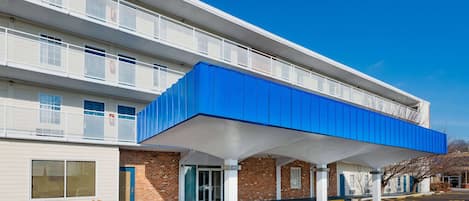 A multi-story hotel with a covered outdoor area, a brick facade, and a parking lot.