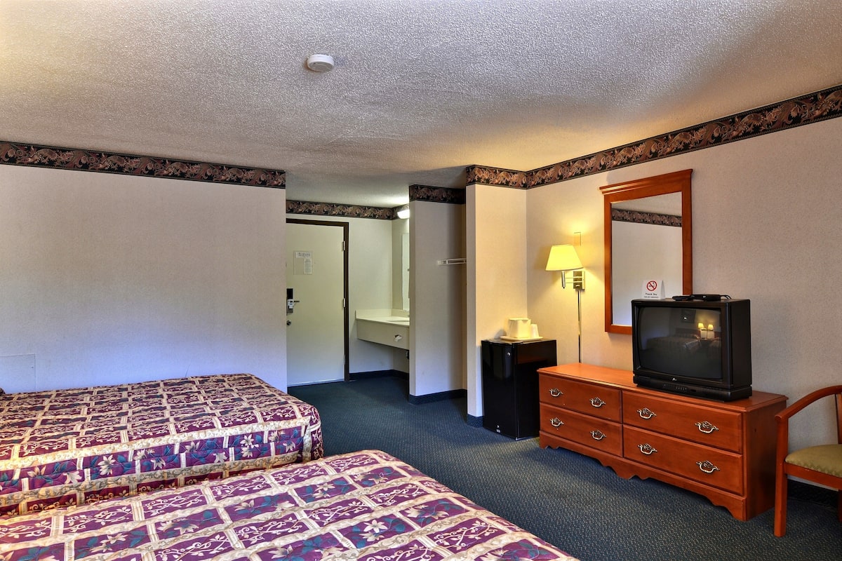 A hotel room with two beds, a dresser with a television, a mirror, and a door leading to a bathroom.