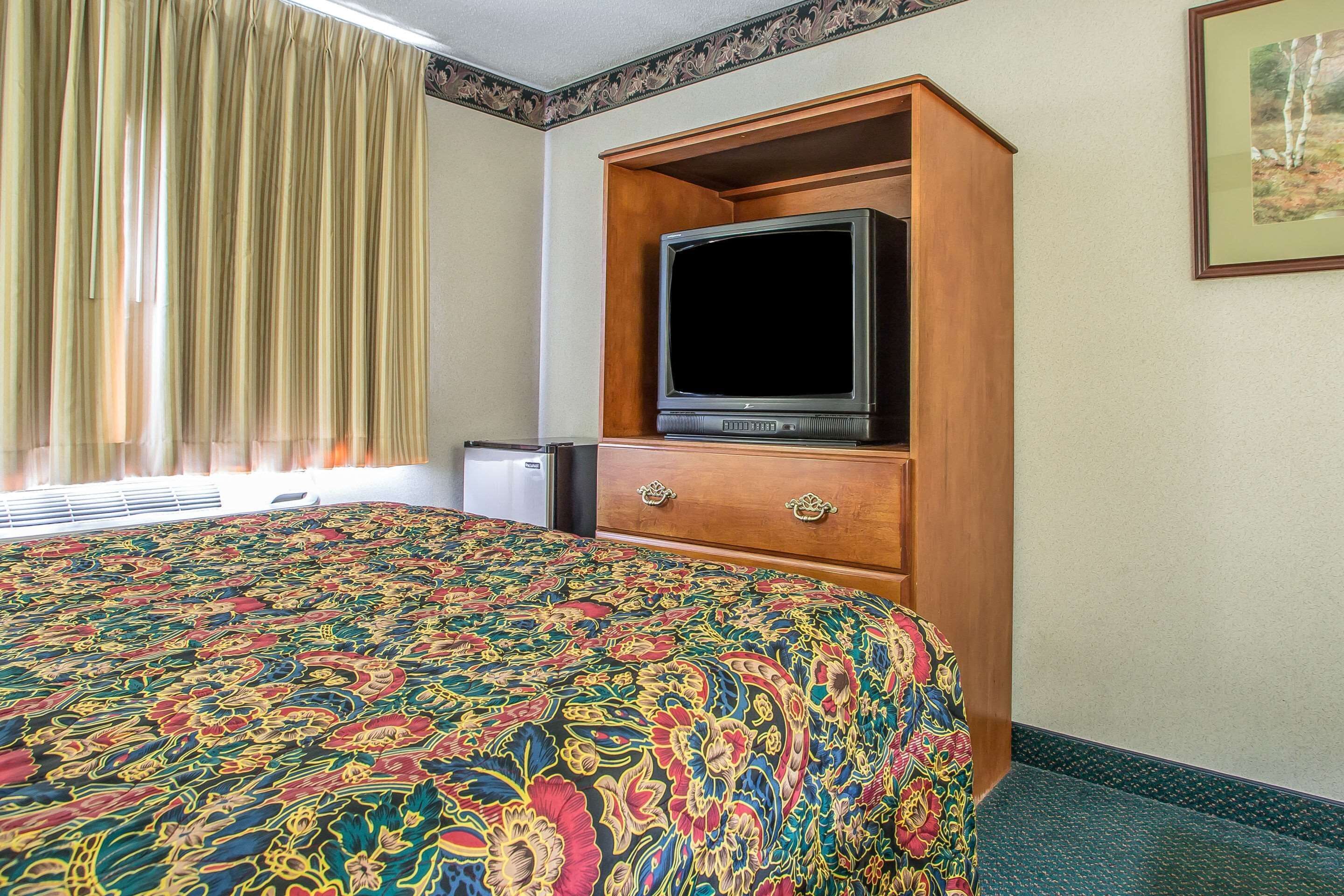 Une chambre d’hôtel avec un grand lit, un téléviseur posé sur un meuble en bois et une fenêtre avec des rideaux.