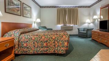 A hotel room with a large bed, two chairs, a dresser, a television, and framed pictures on the wall.