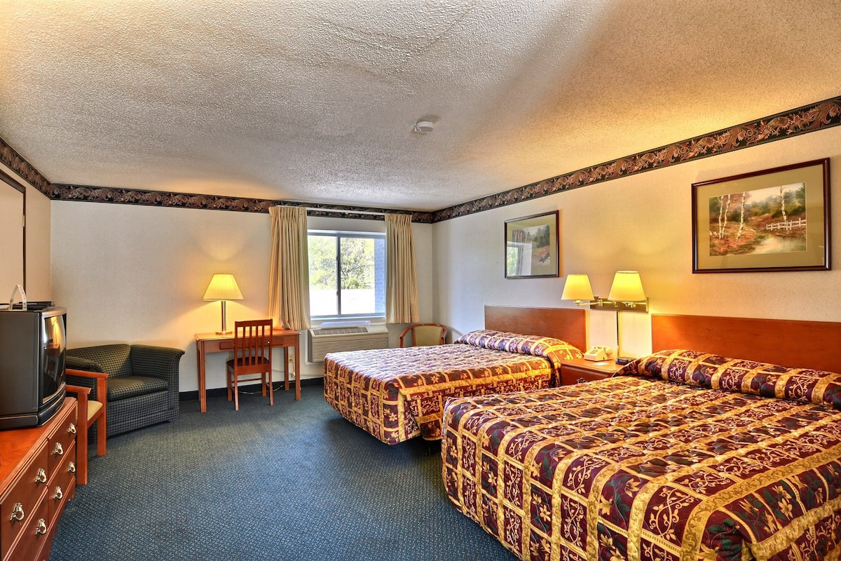 A hotel room with two beds, a desk, a chair, a television, and a window with curtains.