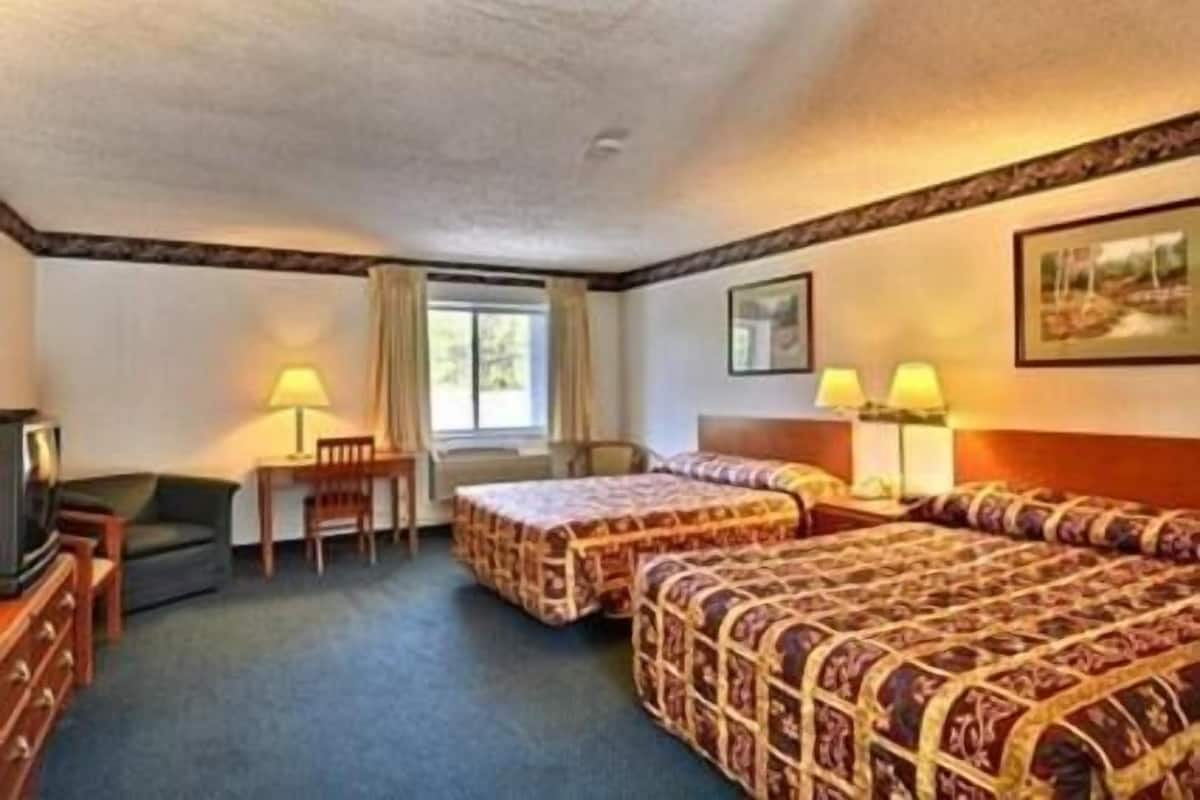 A hotel room with two beds, a desk with a chair, a television, and a window with curtains.
