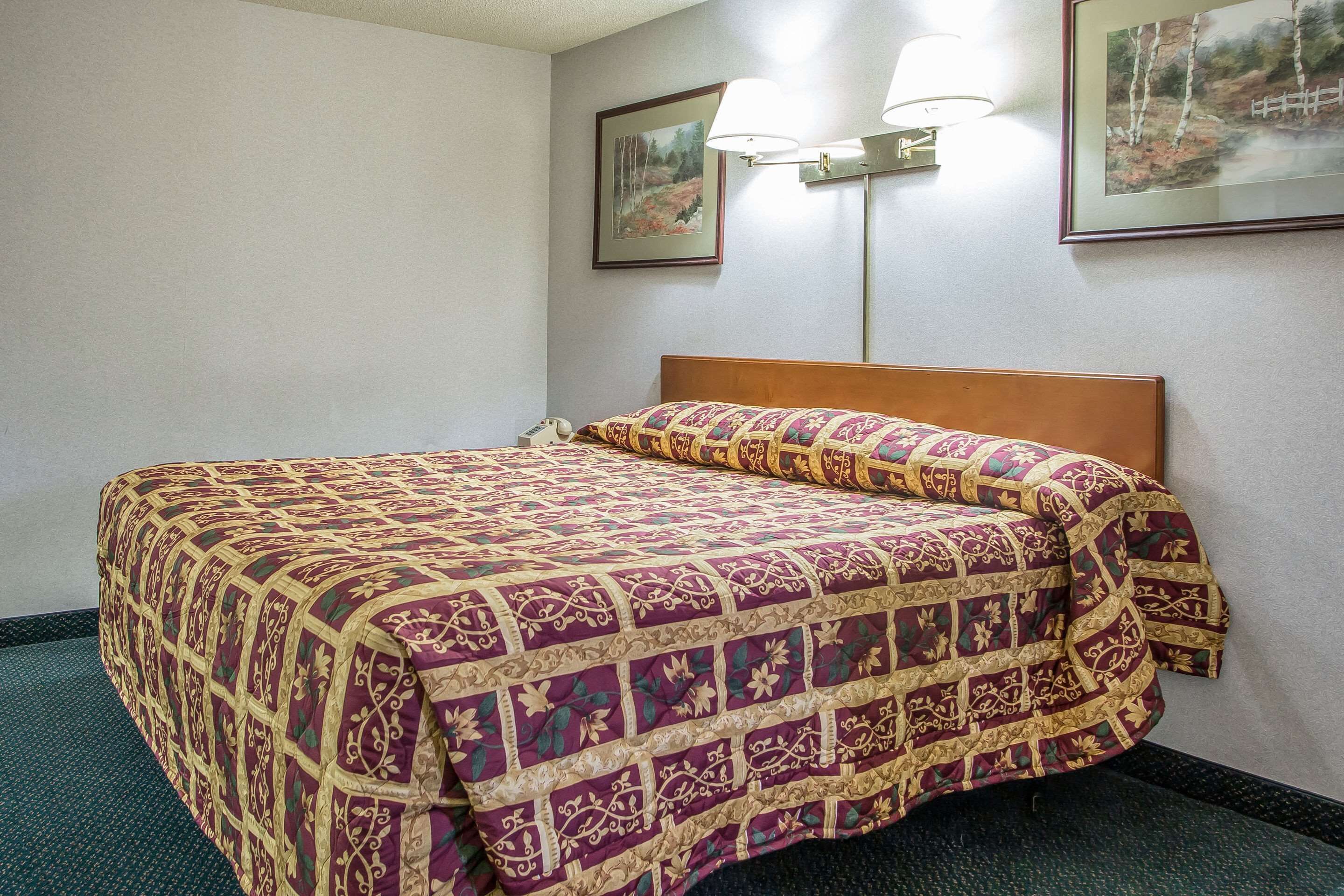A hotel room with a neatly made bed, two wall-mounted lamps, and framed pictures on the walls.