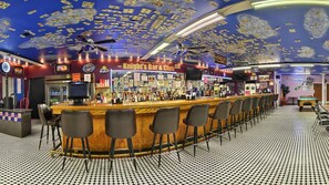 En bar med en lang bardisk, flere stole og et loft pyntet med dollarsedler.