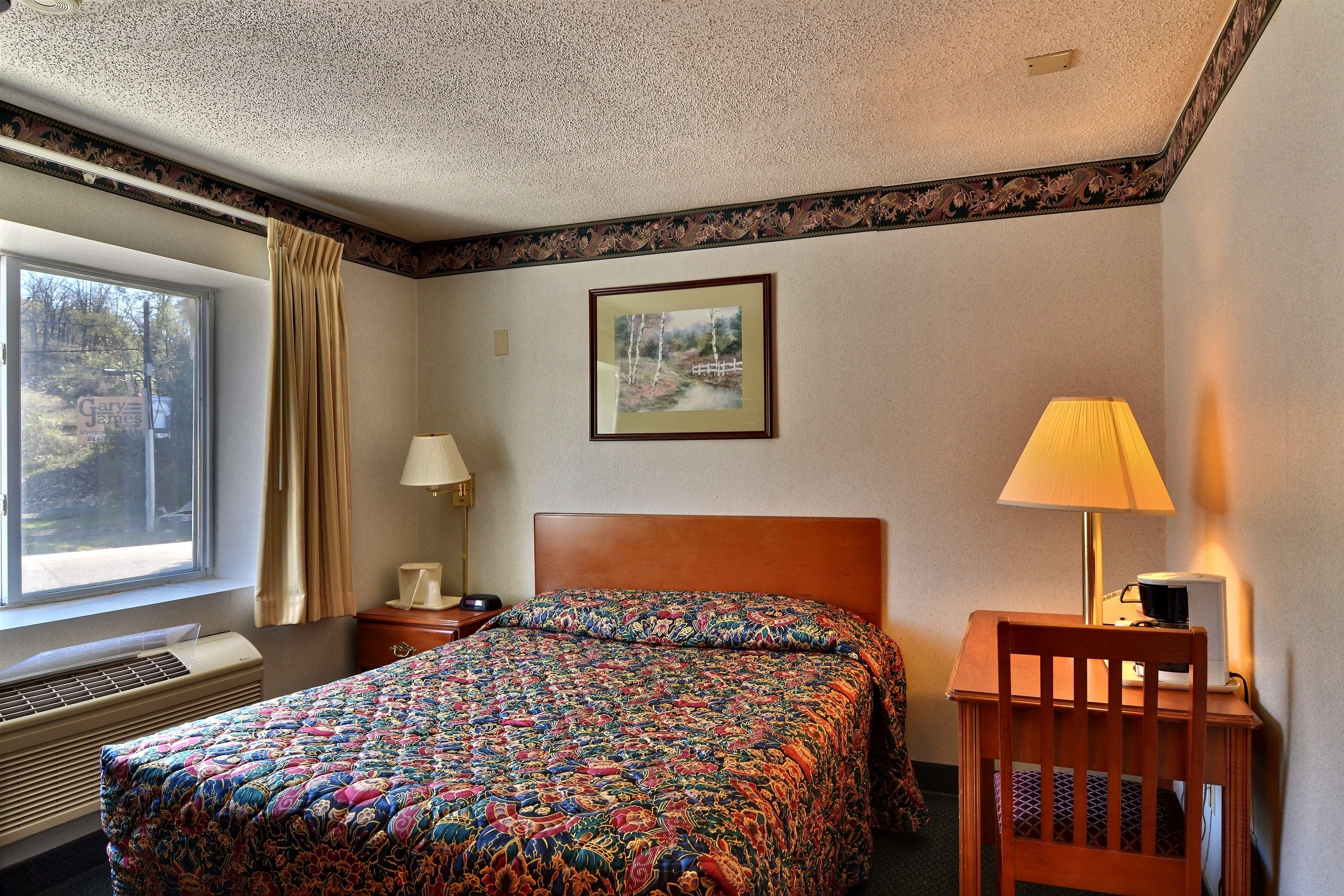 Une chambre d’hôtel avec un grand lit, un bureau avec une lampe, un tableau au mur et une fenêtre avec des rideaux.