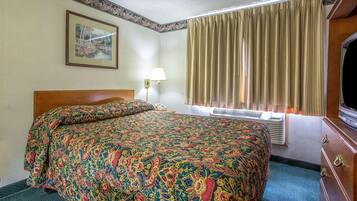 Habitación de hotel con una cama grande, una lámpara de noche, un cuadro enmarcado en la pared, una ventana con cortinas y un tocador con espejo.