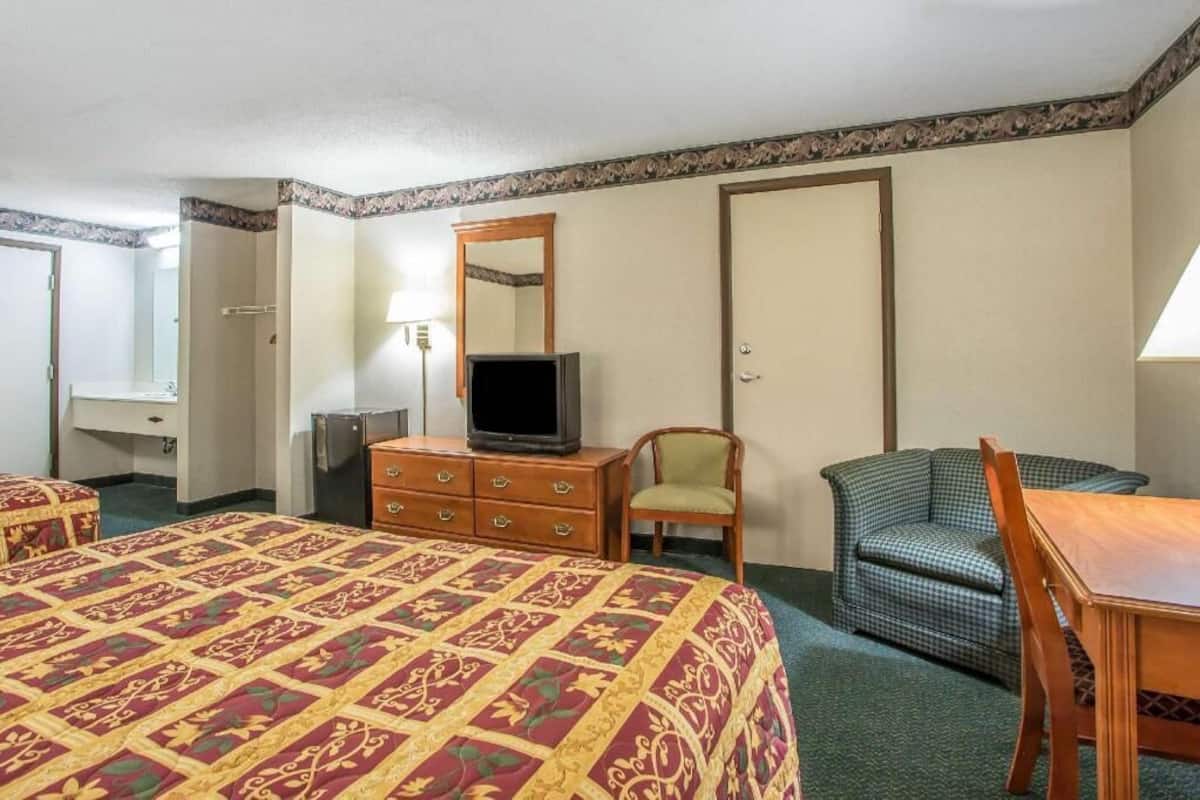 A hotel room with a bed, a dresser, a television, a chair, and a desk.