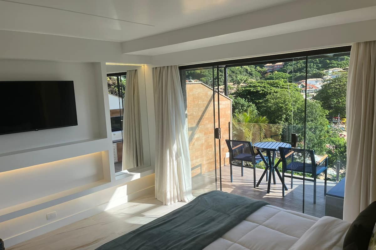A modern bedroom with a large bed, a TV mounted on the wall, and a balcony with a table and chairs.