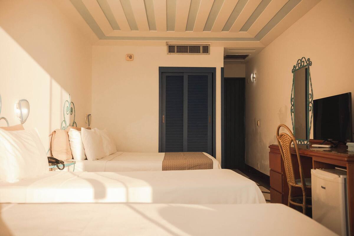 A hotel room with two beds, a desk, a chair, a television, and a wardrobe.