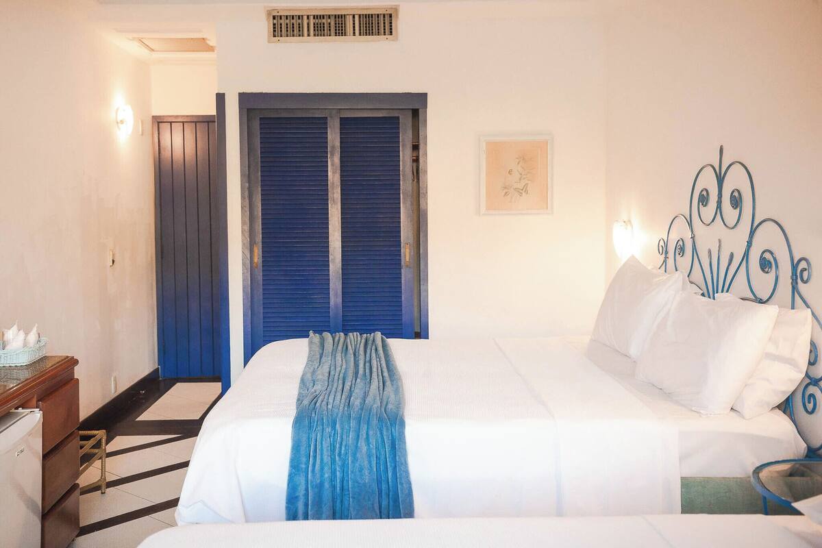 A hotel room with a large bed, a wooden dresser, a desk, and a blue door.