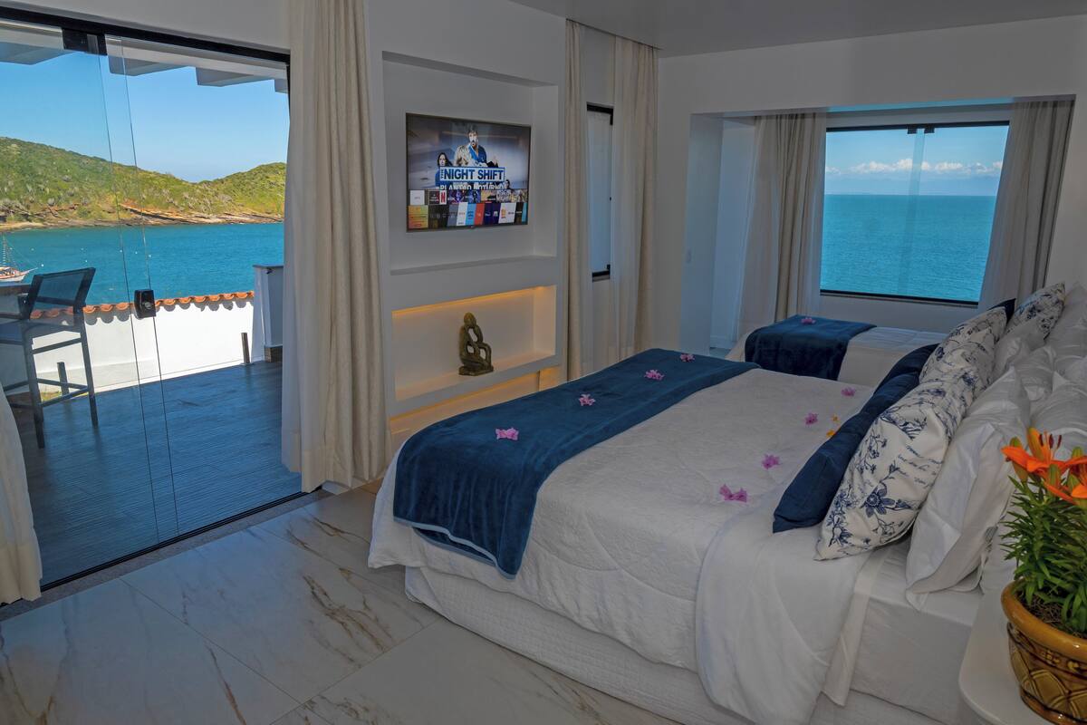 A bedroom with a bed, a TV, and a view of the sea.