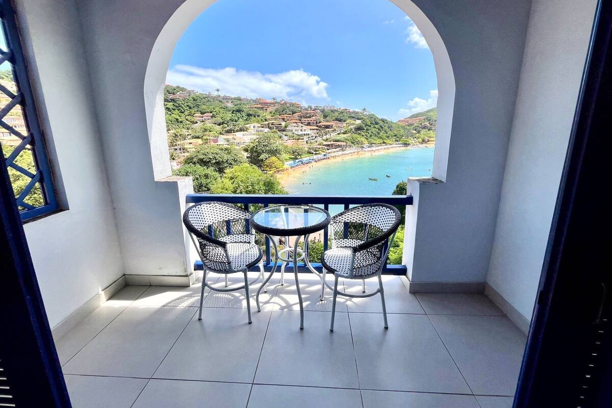 A balcony with two chairs and a table, overlooking a coastal landscape with buildings and greenery.