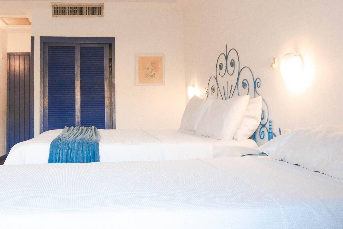 A hotel room with a large bed, a blue-framed door, a wall-mounted light fixture, and a framed picture.