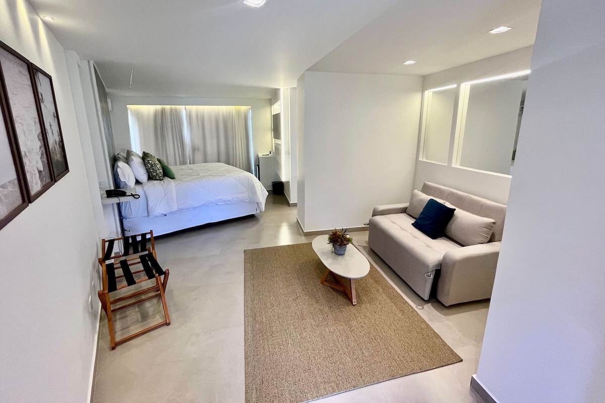 A modern hotel room with a large bed, a sofa, a small coffee table, and a desk.