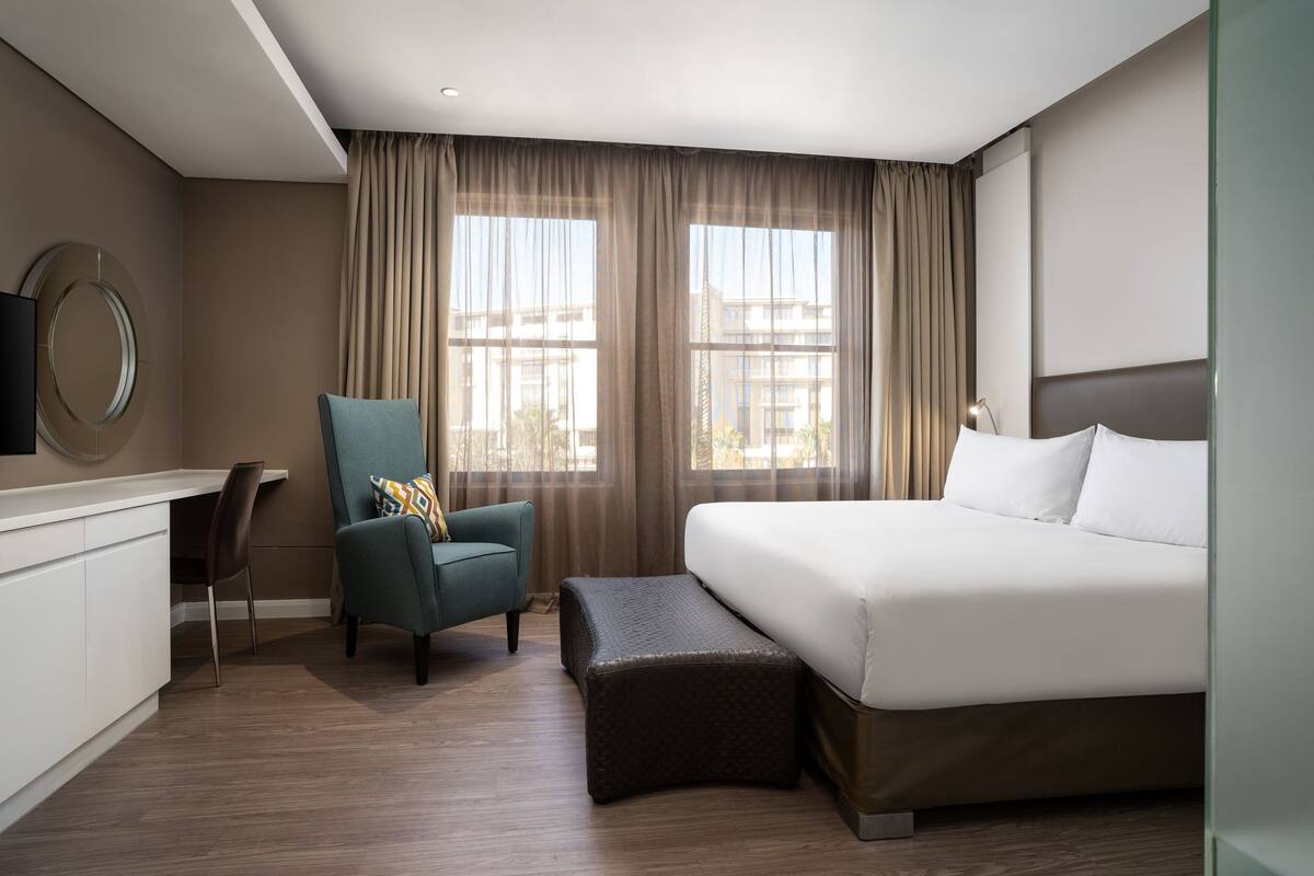 A hotel room with a bed, a desk, a chair, and a large window with curtains.