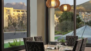 A dining area with a table set for four, large windows offering a view of buildings and greenery. - Protea Hotel by Marriott Cape Town Waterfront Breakwater Lodge (Cape Town)