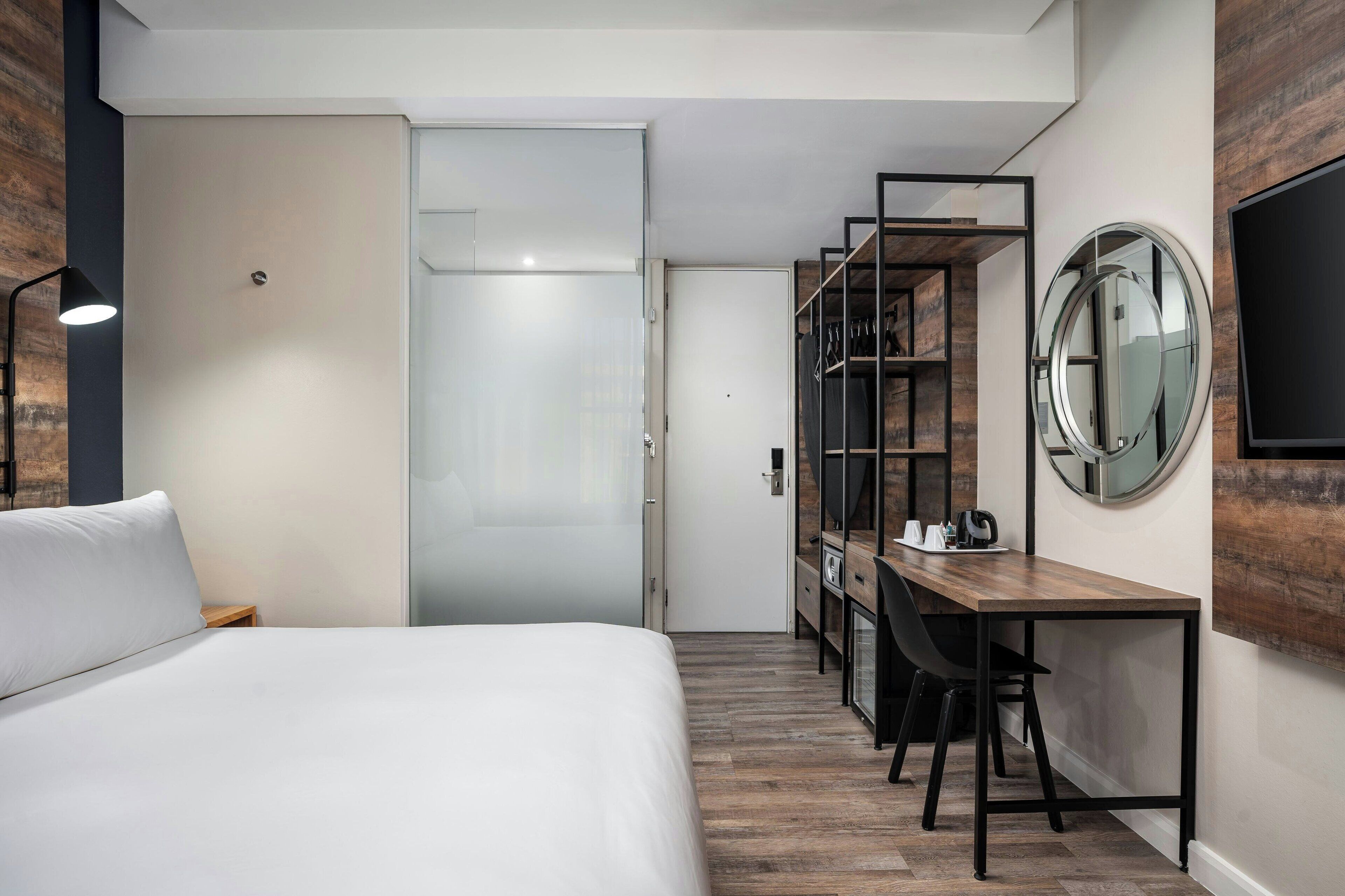 Una camera d'albergo con un letto, una scrivania, una sedia, un armadio e uno specchio rotondo appeso al muro.