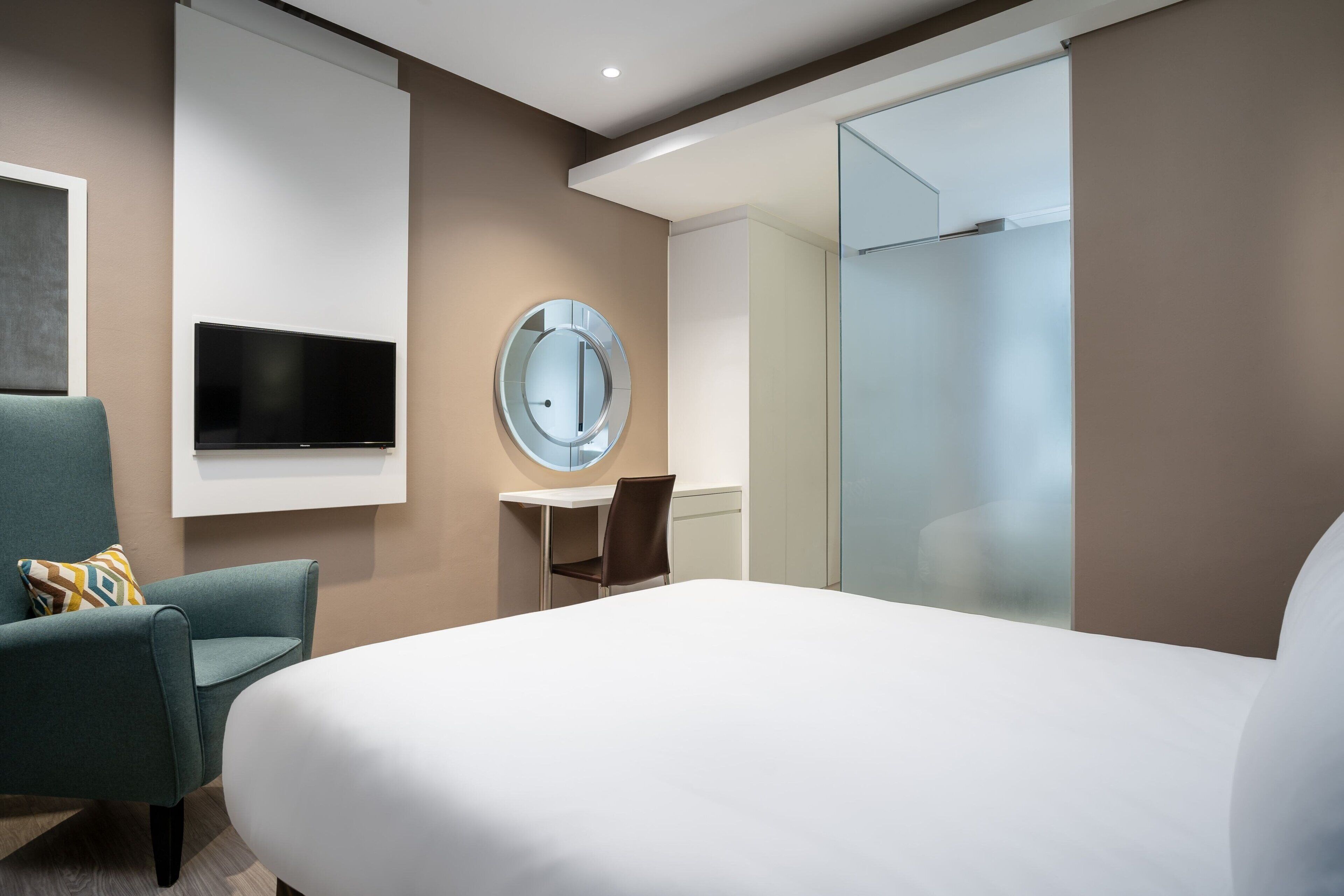Een moderne hotelkamer met een groot bed, een bureau met stoel, een televisie en een ronde spiegel.