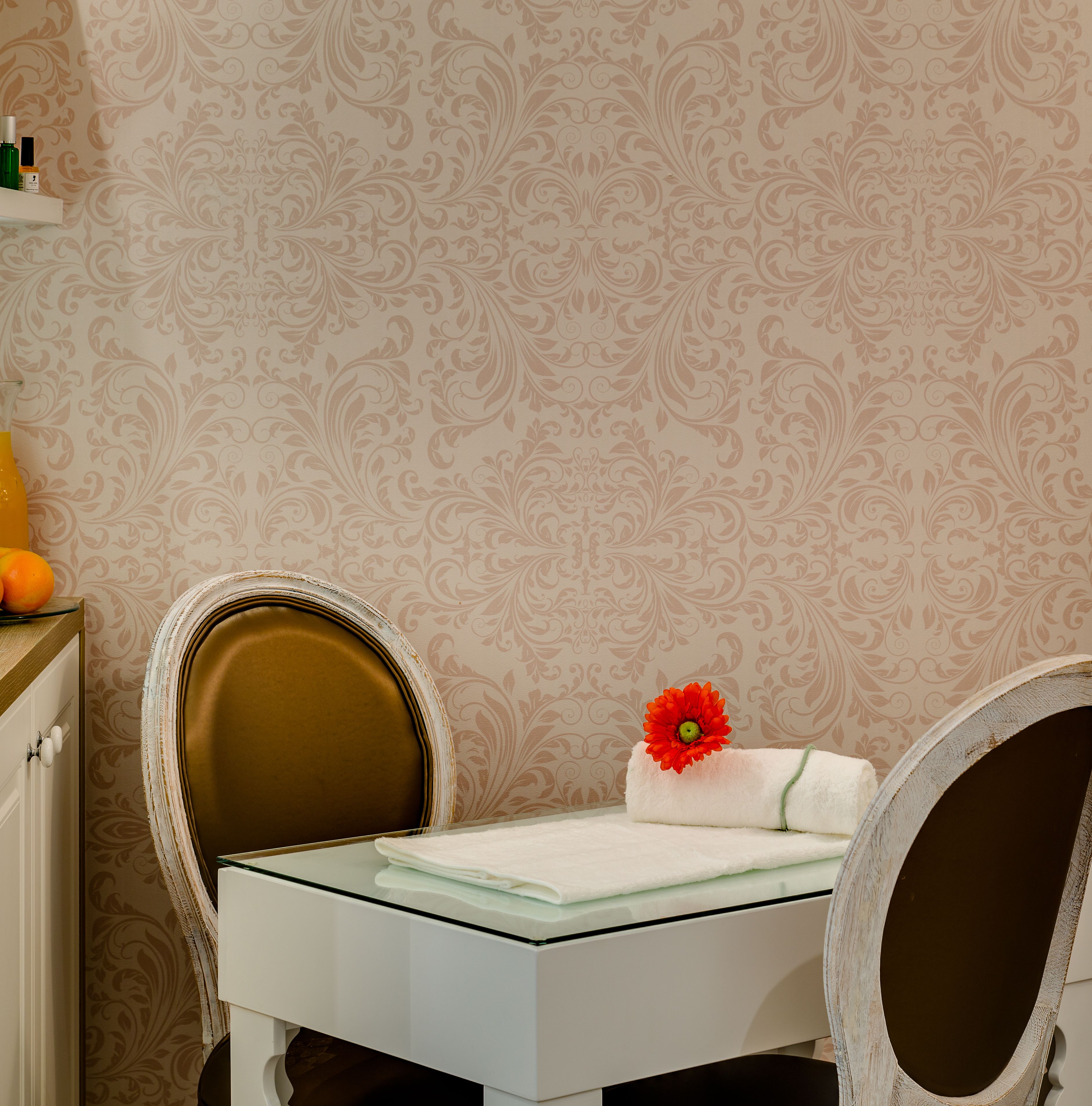 A bathroom with a white vanity, a mirror, and a towel with a red flower. There is a shelf with toiletries and a glass of orange juice.