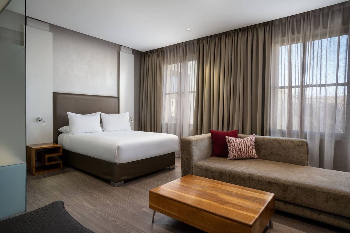 A hotel room with a bed, a sofa, a wooden coffee table, and a nightstand.