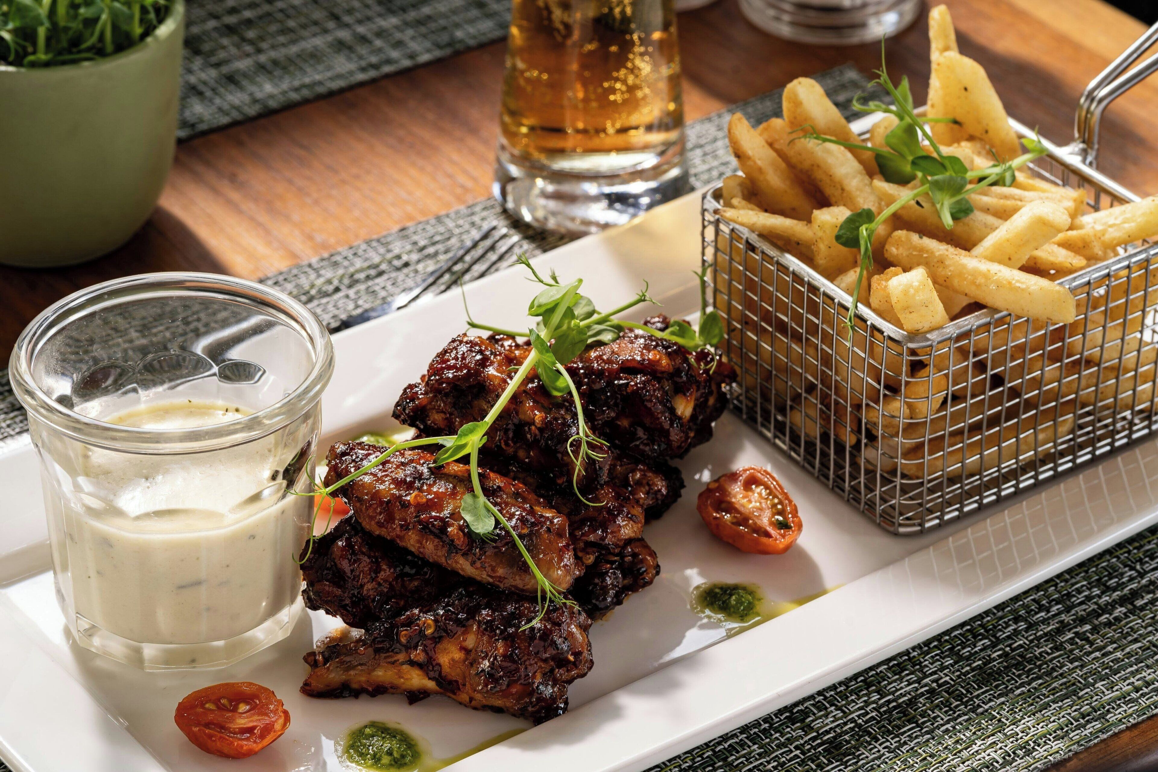 Une assiette d’ailes de poulet grillées, un verre de bière et un panier de frites.