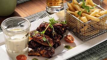 Une assiette d’ailes de poulet grillées, un verre de bière et un panier de frites.
