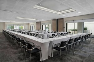 A conference room with long tables and chairs, large windows, and a modern ceiling design.