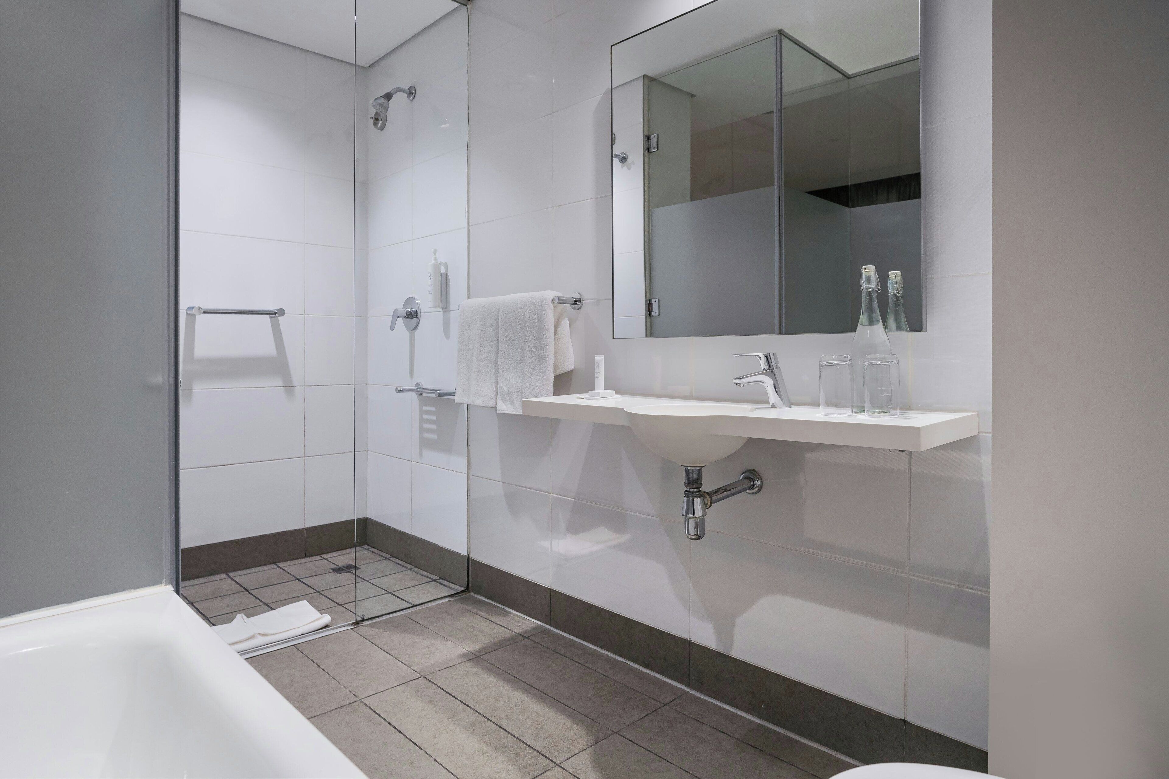 Ein modernes Badezimmer mit einer Duschkabine aus Glas, einem weißen Waschbecken mit Spiegel darüber und einer weißen Badewanne.