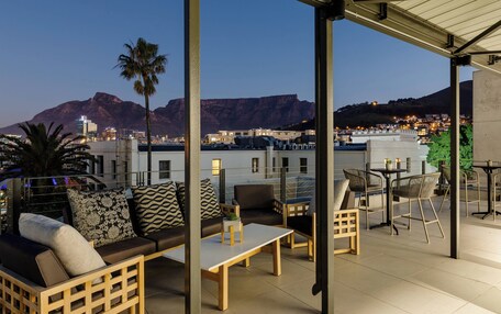 A rooftop terrace with outdoor seating, a palm tree, and a view of a cityscape and mountains.